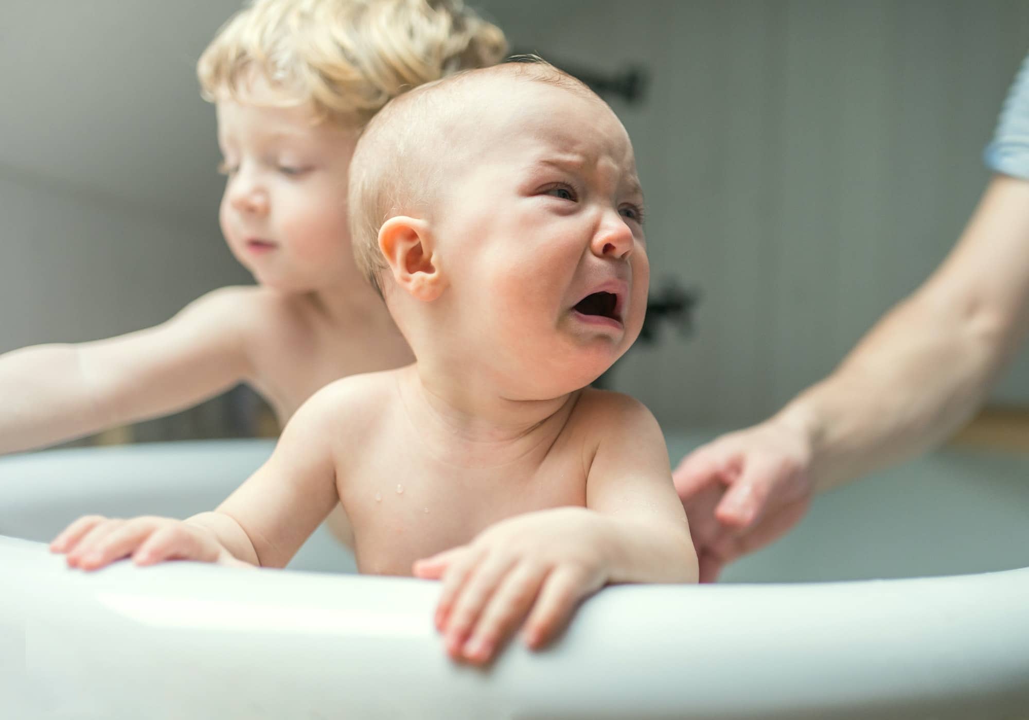 Father washing two unhappy toddlers in the bathroom at home.