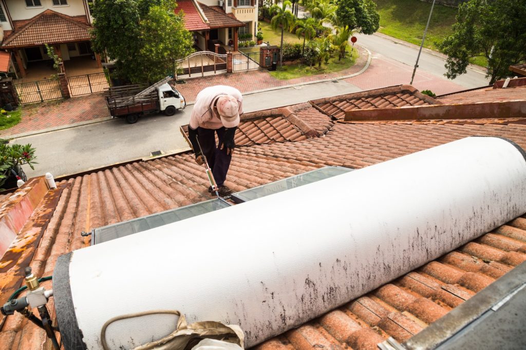 Worker fixing solar water heater on roof during maintenance