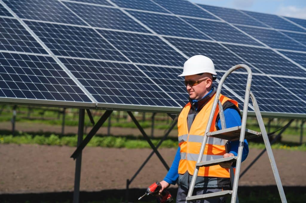 Solar Station Worker Carrying Stepladder. Solar Panel Farm Maintenance Concept